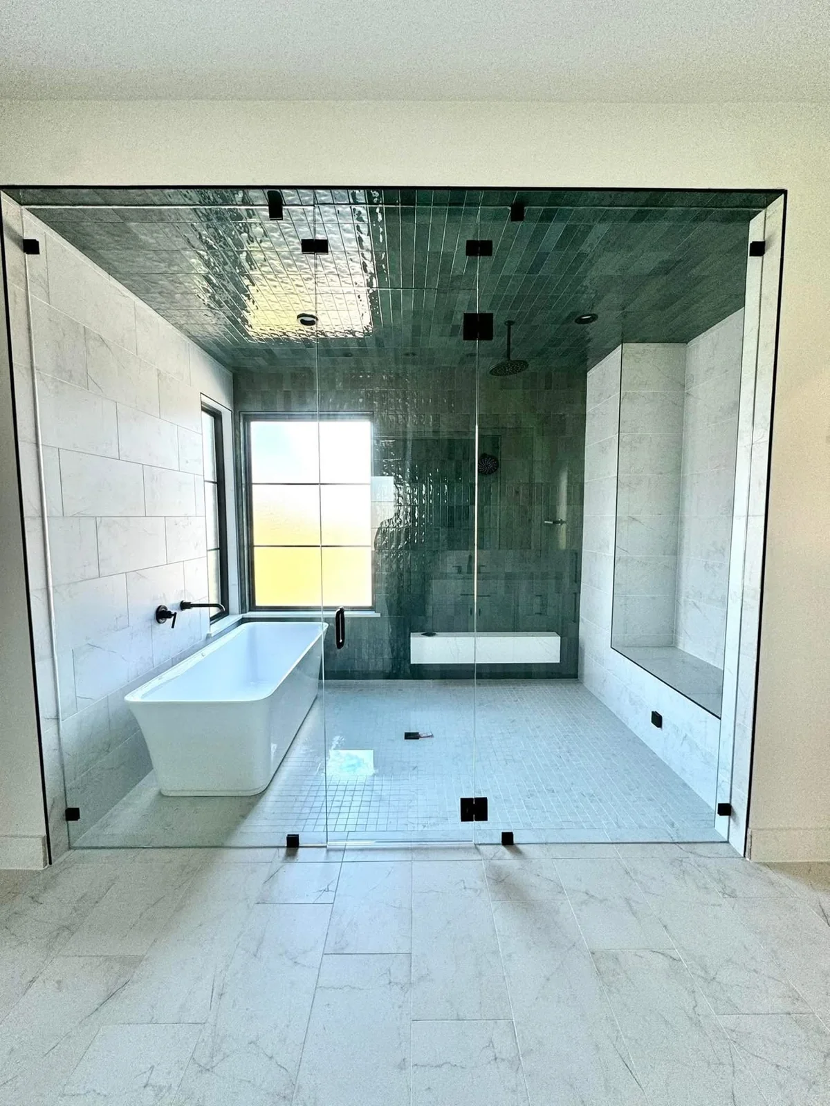 Glass-enclosed shower with green tile and freestanding bathtub